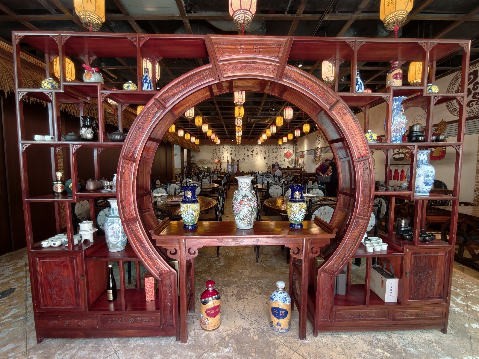 A carved rosewood moon-gate cabinet displaying blue-and-white porcelain vases in the Half Acre dining hall